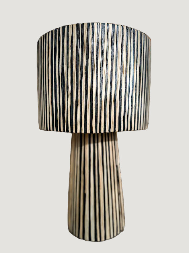 La lampe ILLA séduit par son design épuré et son raffinement artisanal.
Tissée à la main en raphia majoritairement noire, soulignée d’un léger filet de raphia naturel, elle diffuse une lumière douce et enveloppante, parfaite pour créer une atmosphère chic et apaisante.

Idéale sur une table d’appoint, une console ou en lampe de chevet, ILLA apporte une touche contemporaine et authentique à tout type d’intérieur.