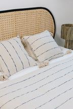 Tissé et confectionné à la main en coton brut sur un métier traditionnel marocain, le plaid INDIRA apporte caractère et authenticité à votre intérieur.

Son élégance réside dans ses rayures indigo sur fond écru, intemporels et raffinés.
Ses finitions soignées, rehaussées de pompons, en font une pièce chaleureuse et unique.