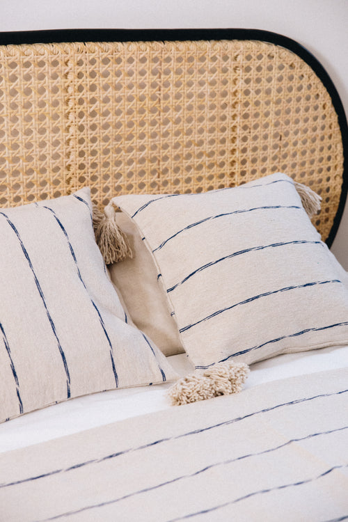 En coton brut tissé et confectionné à la main sur un métier traditionnel marocain, la housse INDI séduit par son élégance épurée.
Ses fines rayures indigo sur fond écru apportent une touche authentique et intemporelle à votre décoration.