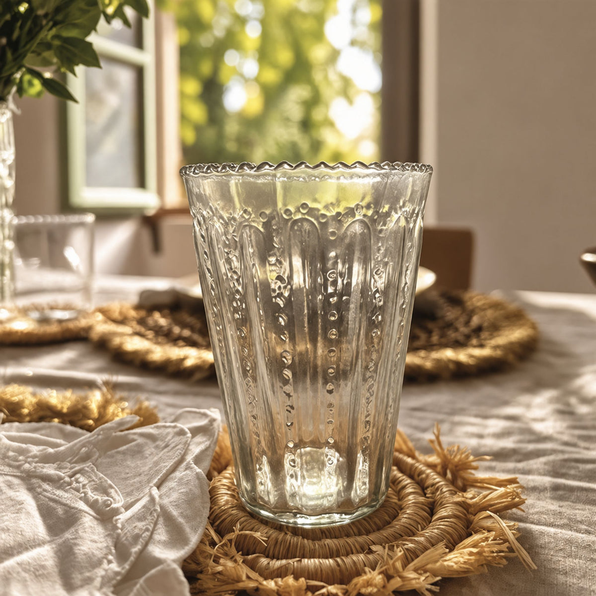 Verre PANTEA soufflé haut à bord ondulé sur un sous-verre en raphia